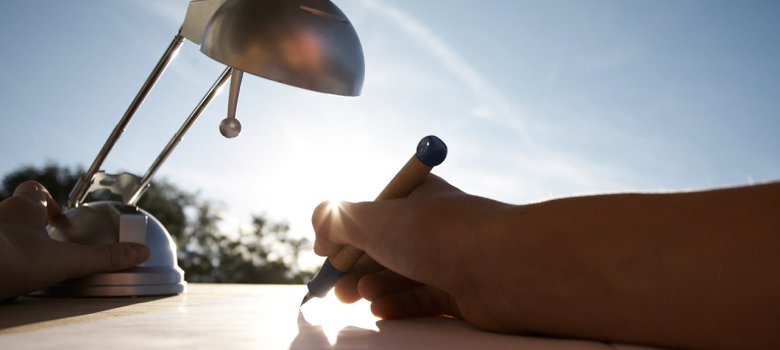 Schreibtisch mit Schreibtischlampe und einer Hand, die etwas aufschreibt